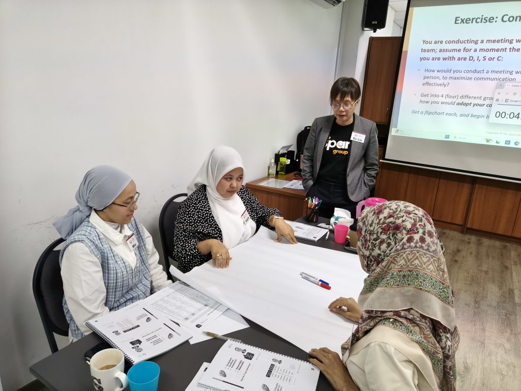 Participants work on presentation on mahjong paper to discuss DISC profile and Coach reviewing the activity with hands behind her